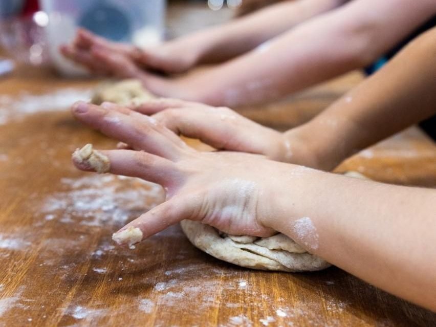 Mãos de crianças abrindo massa de pão sobre a bancada enfarinhada